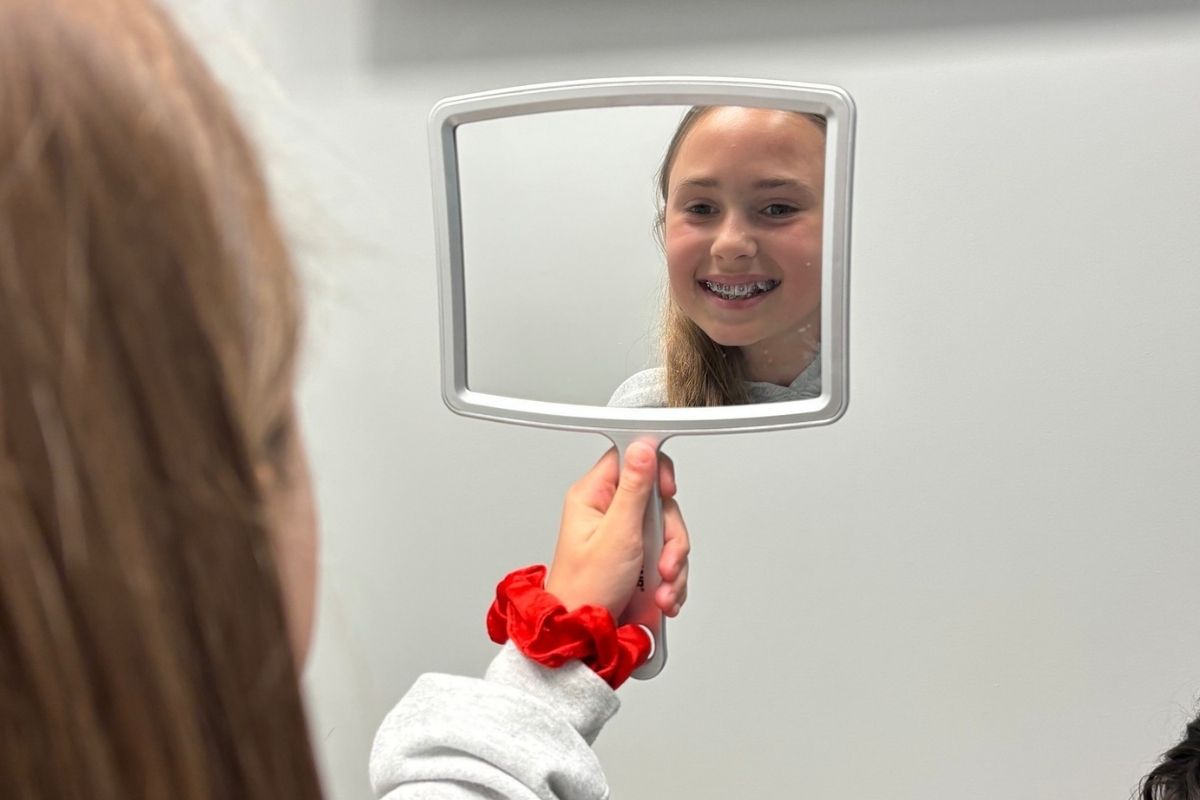 Young patient checking braces in mirror after orthodontic emergency visit in Chesapeake VA near Elizabeth City NC and Moyock NC