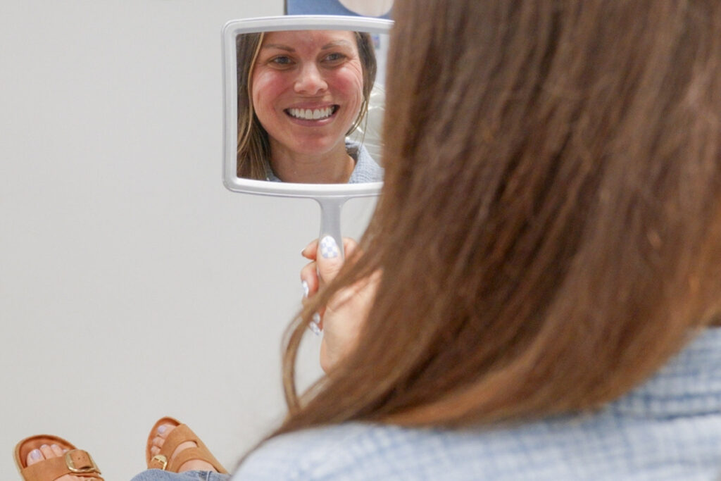 Confident Smile Results – Glass Orthodontics Patient checking smile in mirror after orthodontic treatment in Chesapeake VA at Glass Orthodontics serving Elizabeth City NC and Moyock NC