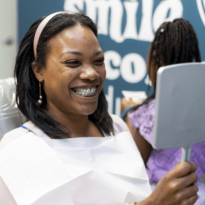 Adult woman smiling with braces while looking in mirror at orthodontic office, illustrating Invisalign versus braces options