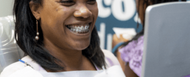 Adult woman smiling with braces while looking in mirror at orthodontic office, illustrating Invisalign versus braces options
