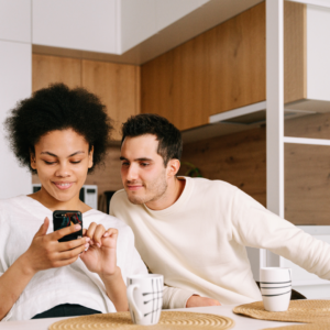 Couple in a modern kitchen smiling while looking at a smartphone, representing excitement about the new website for Glass Orthodontics